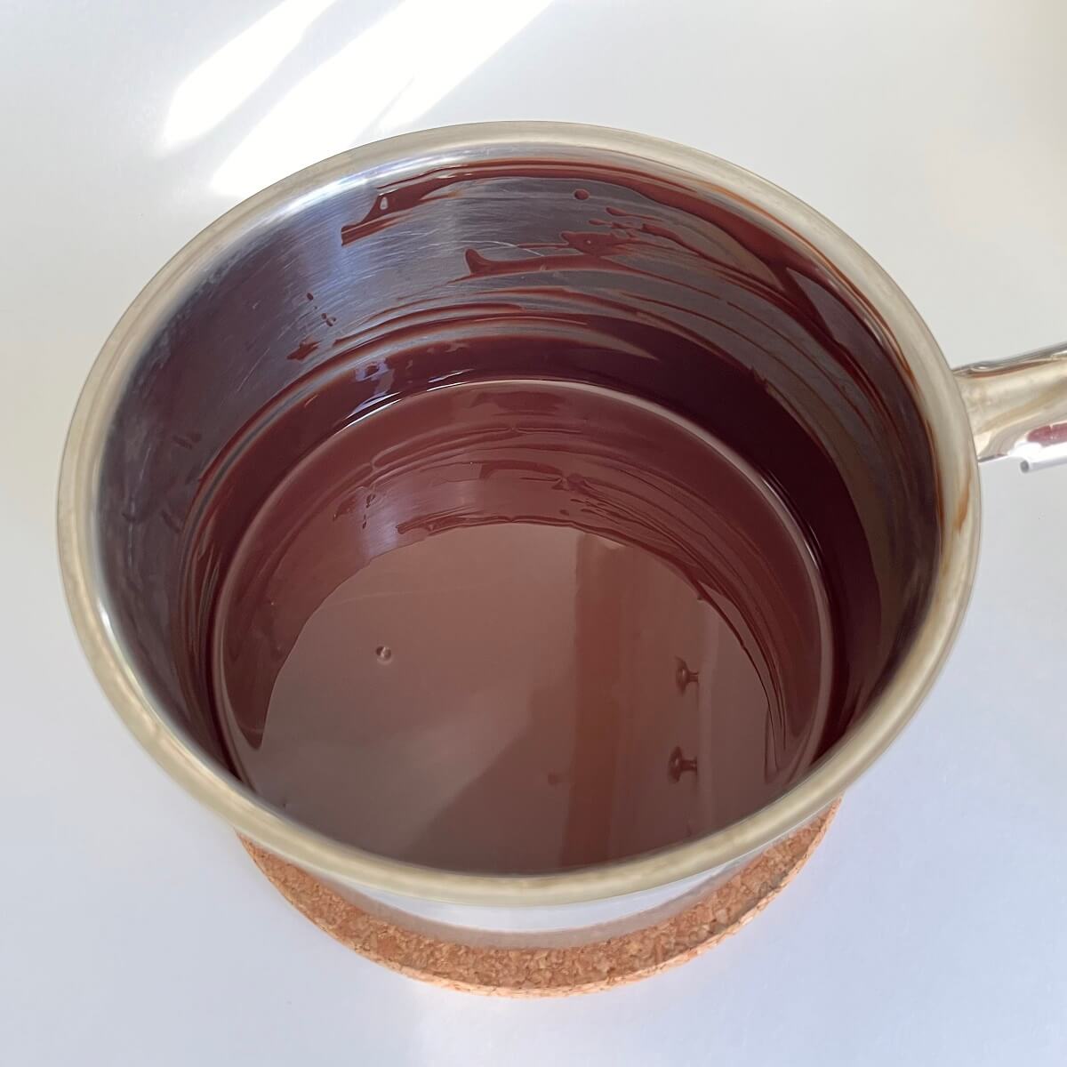 Melted dark chocolate in a steel pot on a cork trivet.