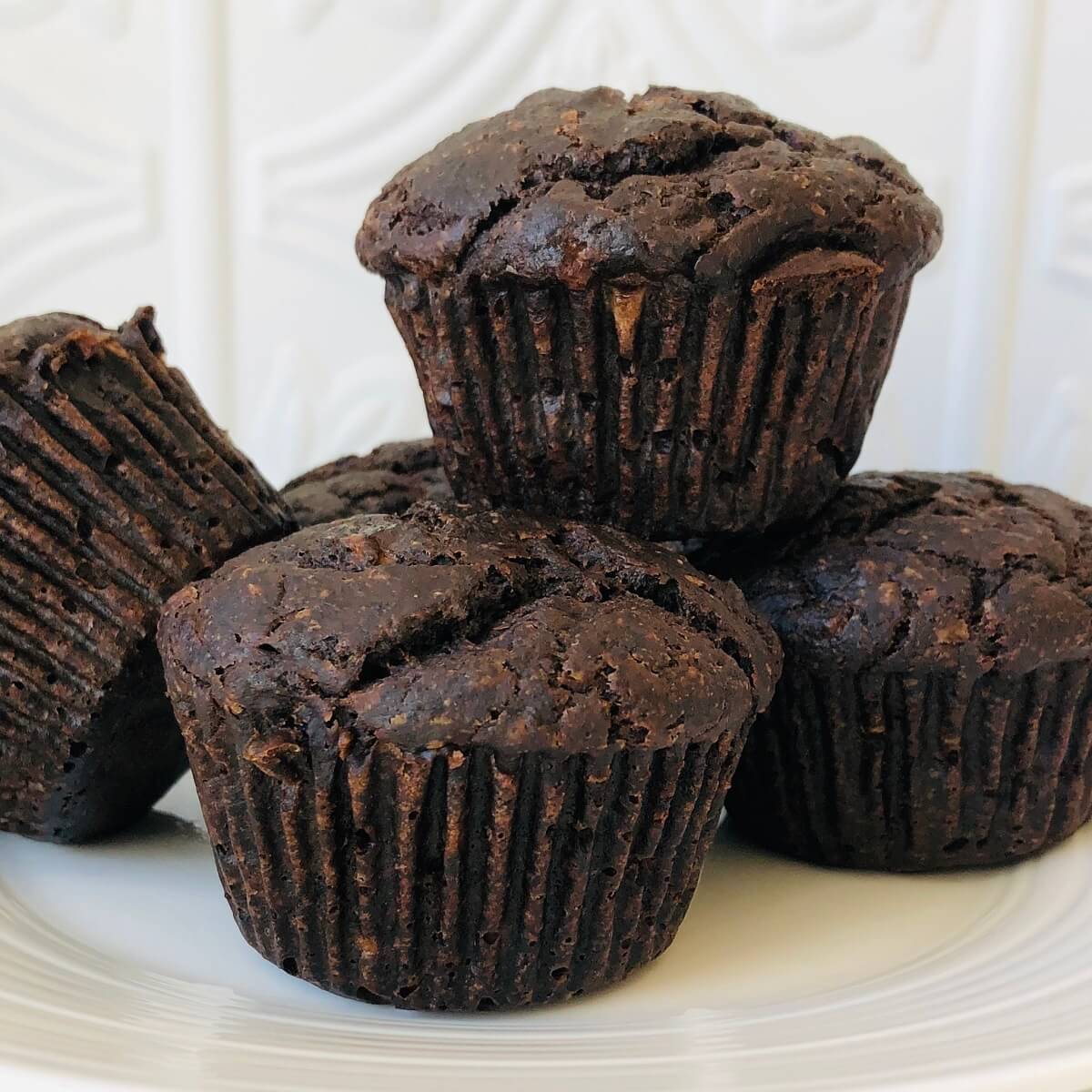 Buckwheat flour chocolate muffins stacked on a white plate.