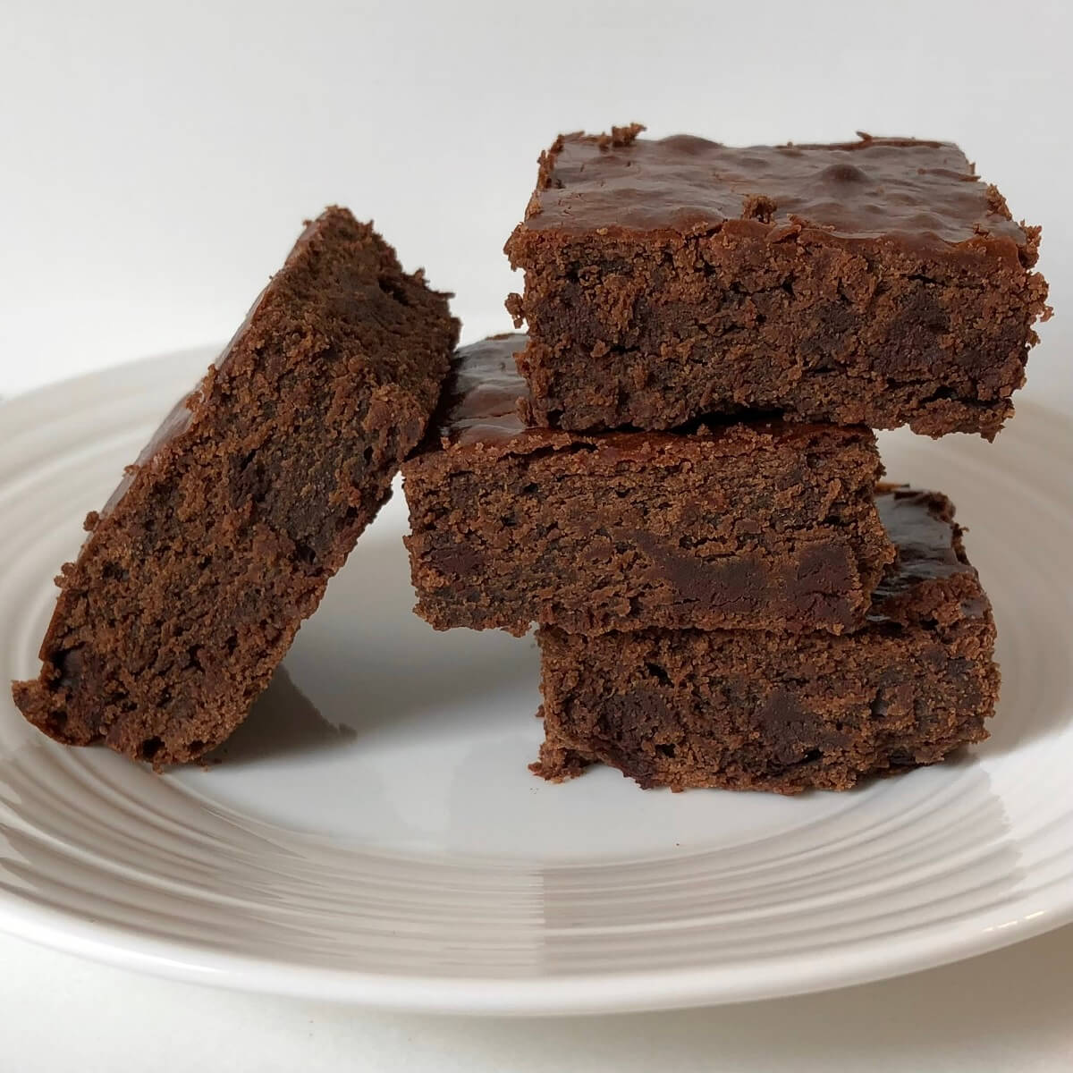 Chocolate brownies made with chickpea flour stacked on a white plate.
