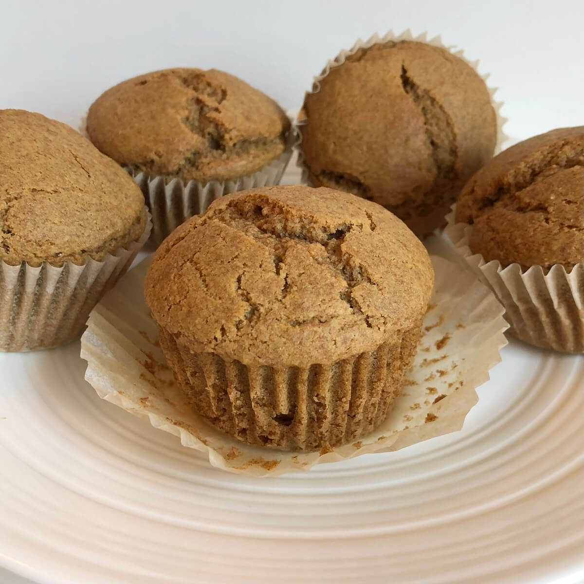 Five muffins made with spelt flour on a white plate.