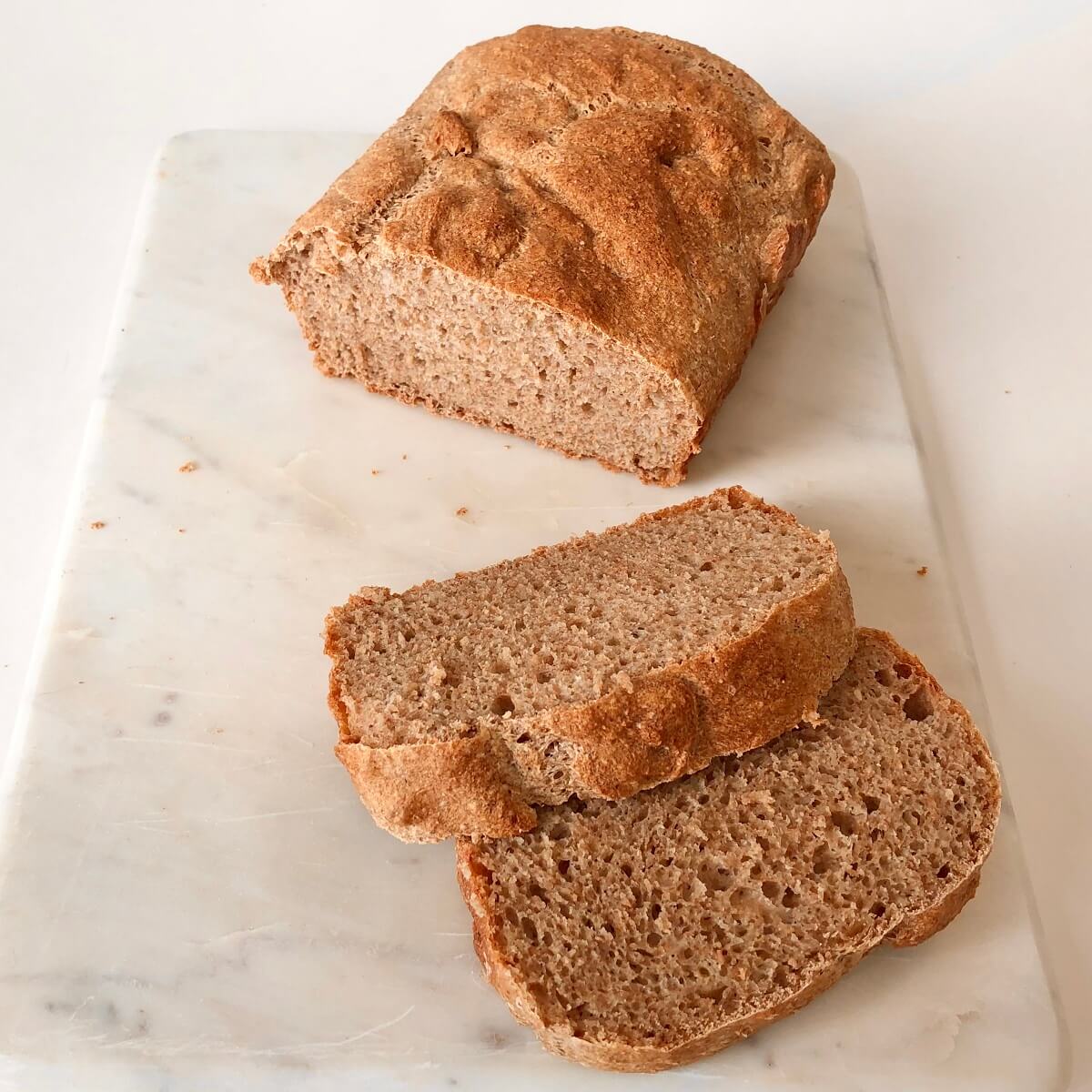 A loaf of homemade whole wheat bread on a marble cutting board with two thick slices cut.