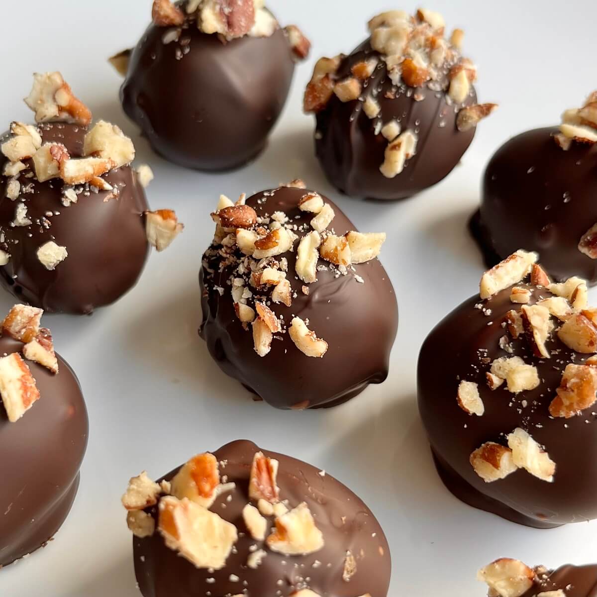 Chocolate covered grapes sprinkled with chopped pecans on a white plate.