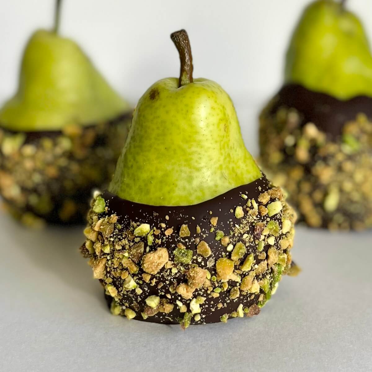 Three chocolate covered pears crusted with chopped pistachios.
