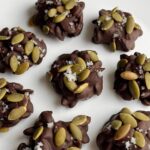 Chocolate covered pumpkin seeds on a white plate.