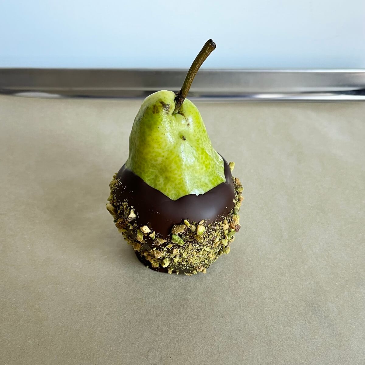 A chocolate dipped pear on a sheet pan lined with parchment paper.