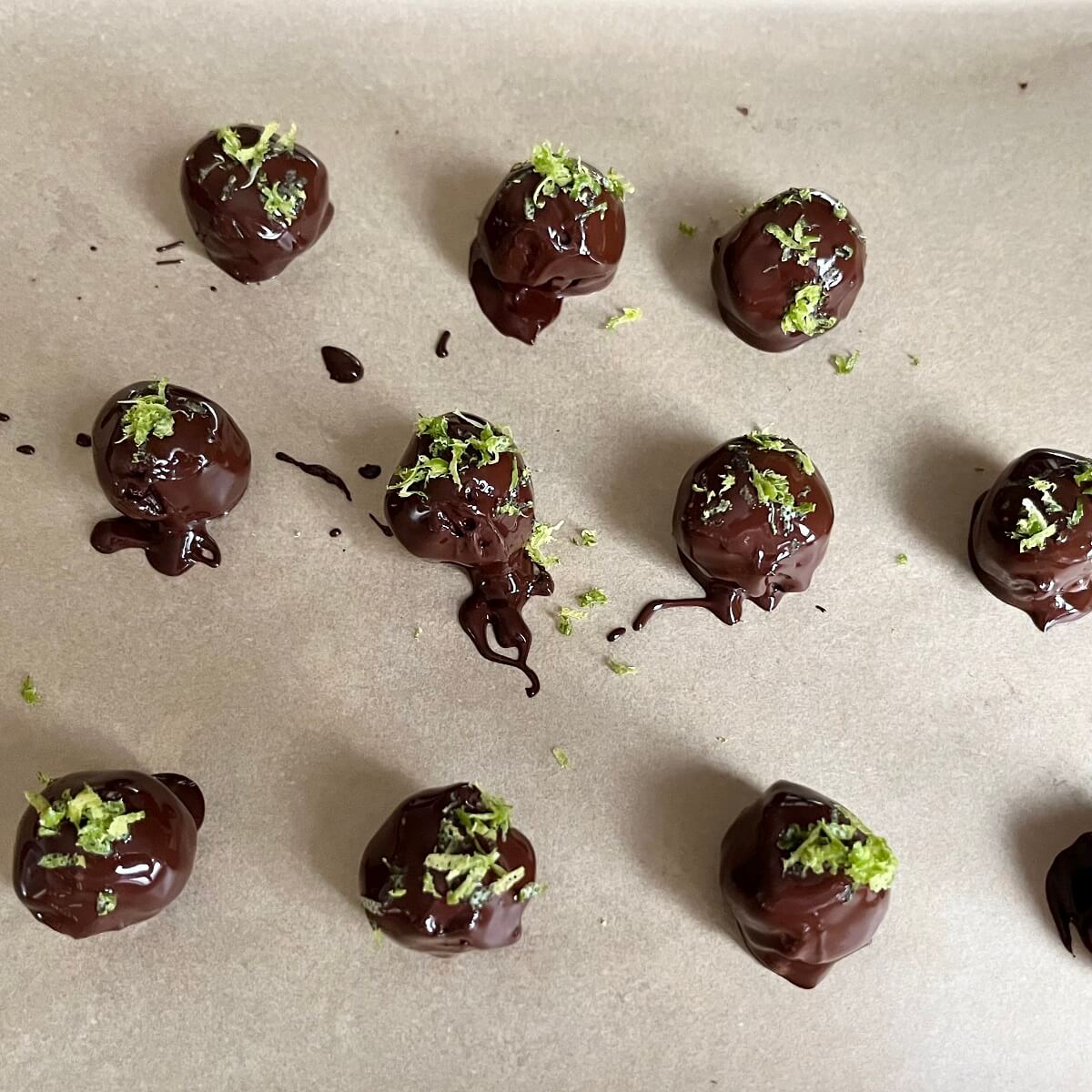 Chocolate lime balls sprinkled with lime zest on a piece of parchment paper.