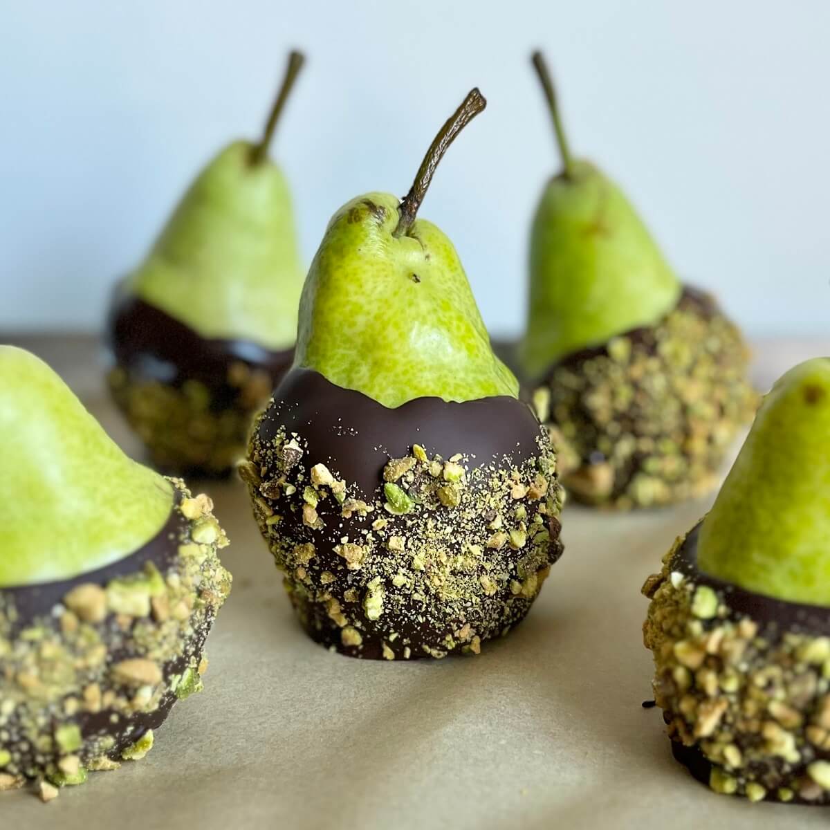 Five chocolate coated pears on a sheet pan lined with parchment paper.