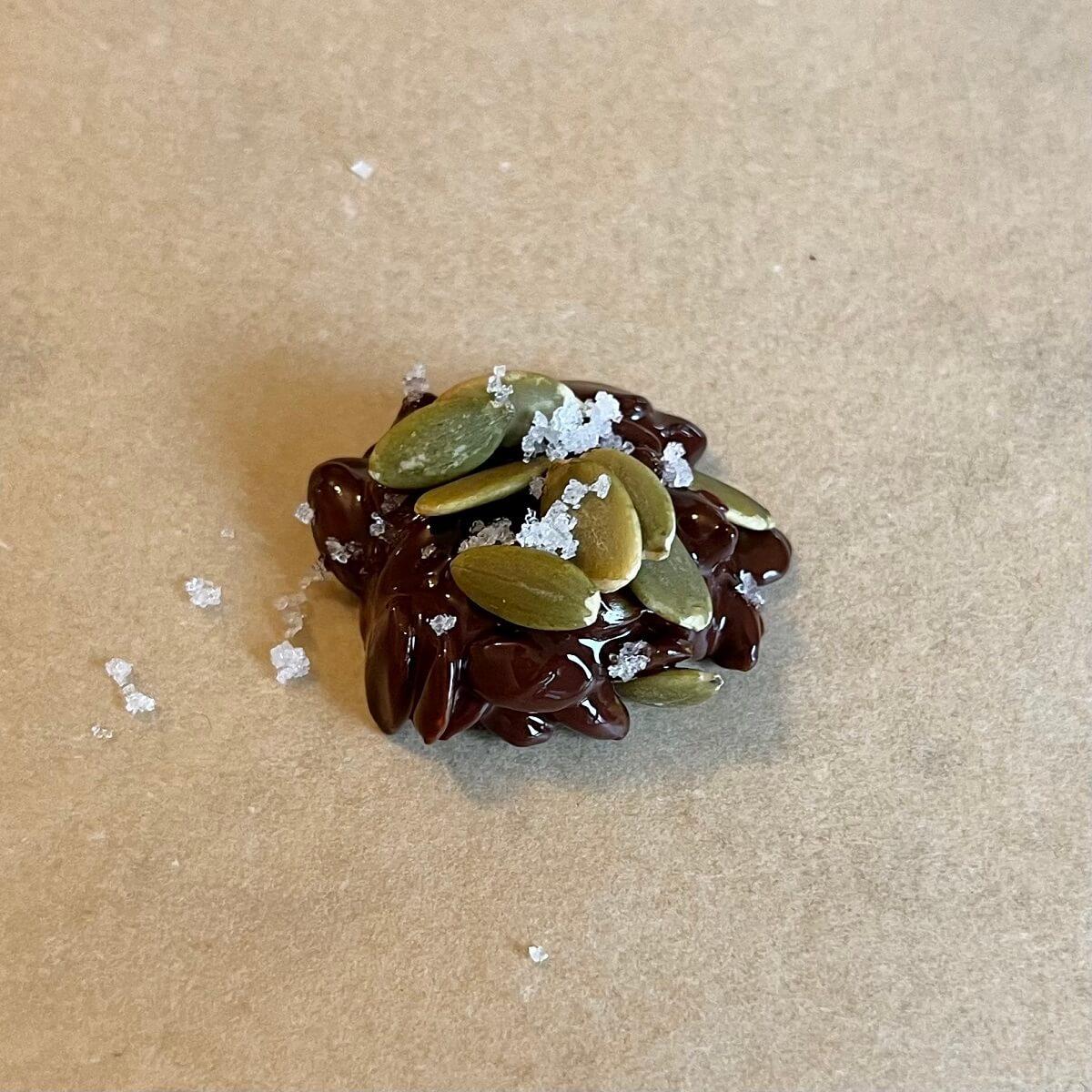 A chocolate pumpkin seed cluster on a piece of parchment paper.