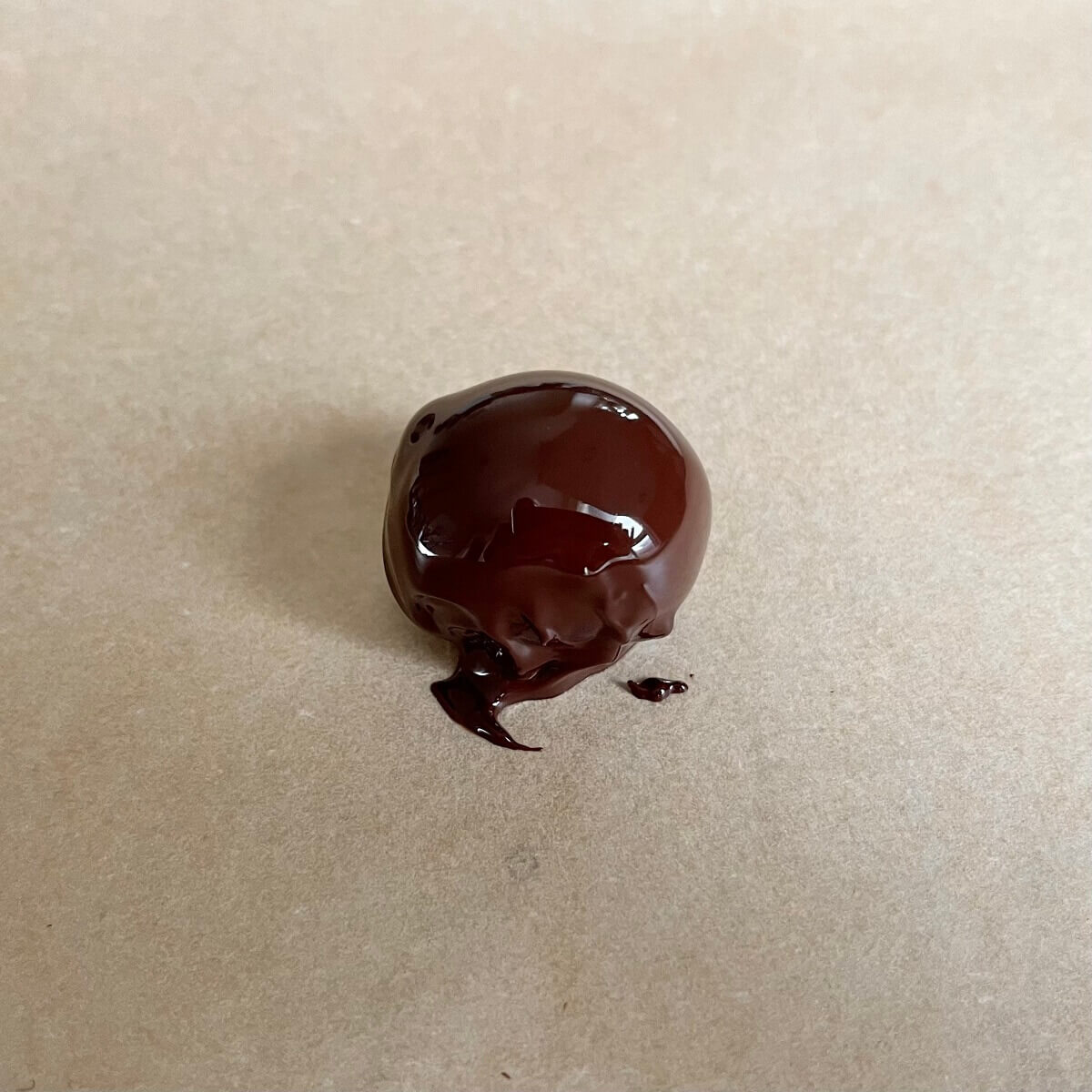 A single dark chocolate coated grape on a piece of parchment paper.