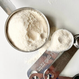 A steel measuring cup and spoons filled with coconut flour.