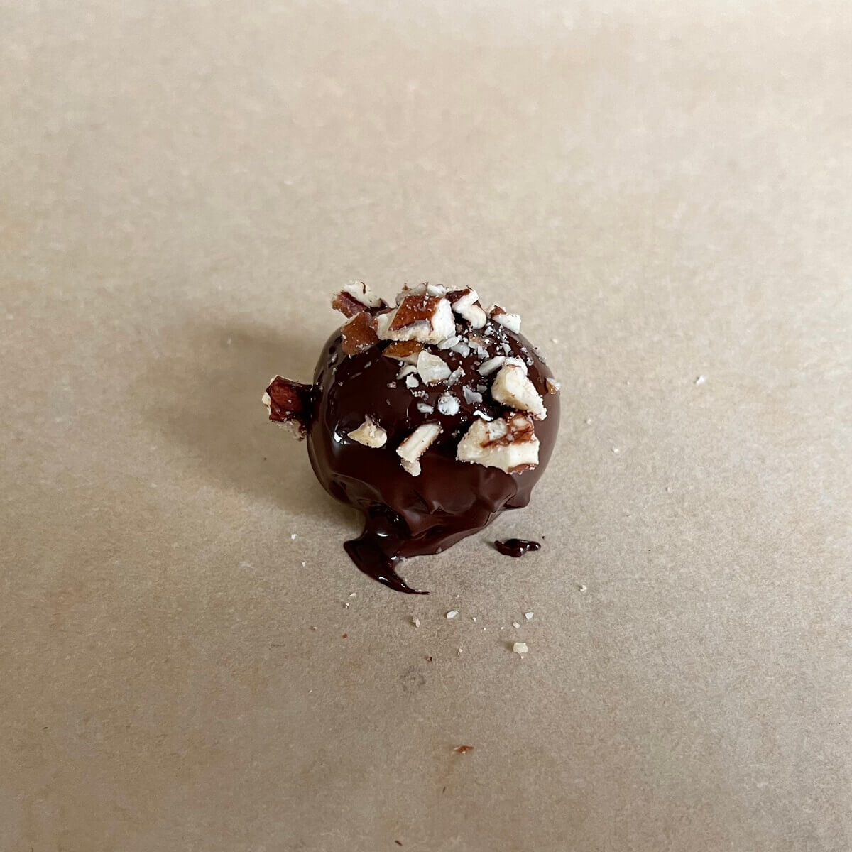 A chocolate dipped grape sprinkled with finely chopped nuts on a piece of parchment paper.