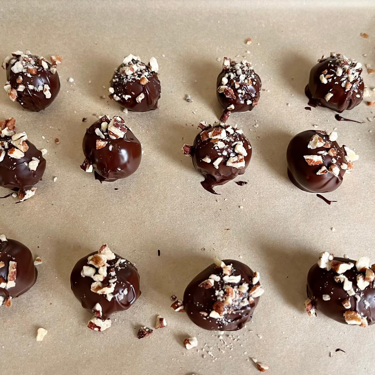 Grapes coated in chocolate and sprinkled with nuts on a sheet pan lined with parchment paper.