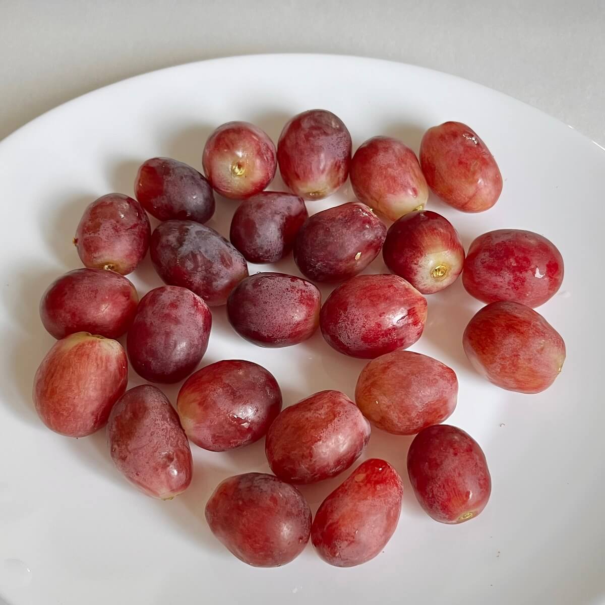 Twenty-four red grapes on a white plate.