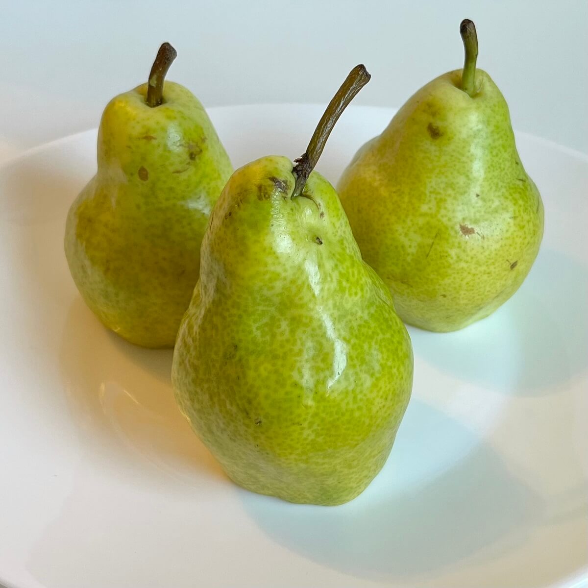 Three fresh pears on a white plate.