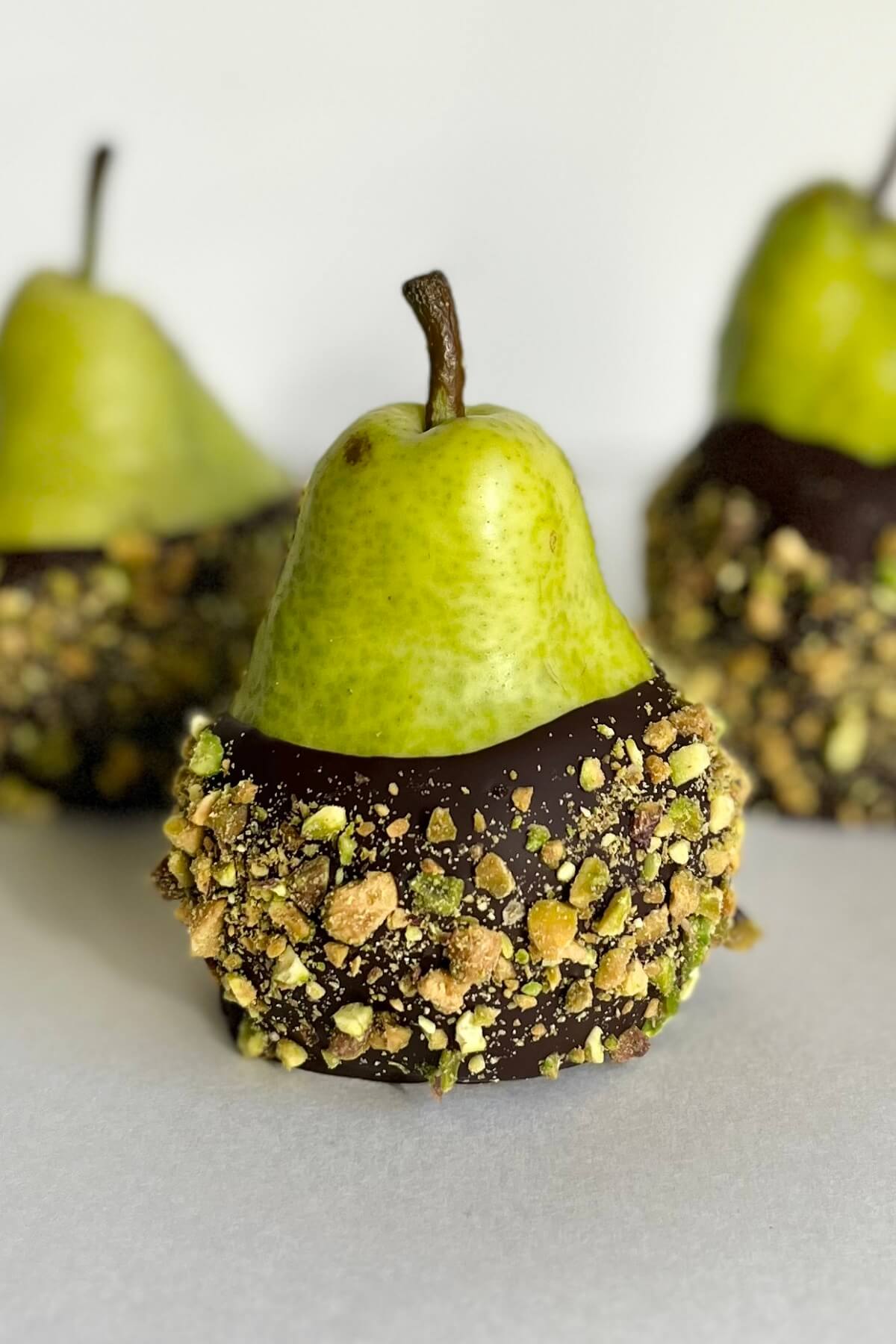 Three pistachio crusted chocolate pears against a white background.