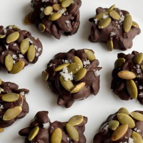 Chocolate pumpkin seed clusters on a white plate.