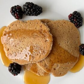 Three pancakes on a plate with fresh blackberries and maple syrup.