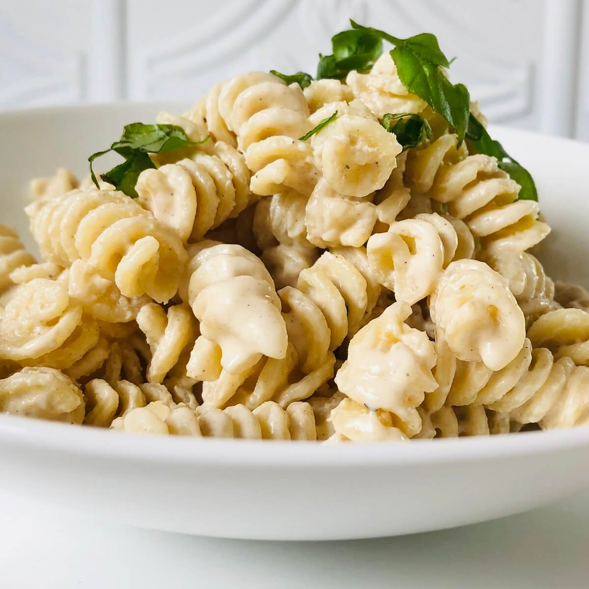 Creamy vegan pasta with fresh basil sprinkled on top in a white bowl.