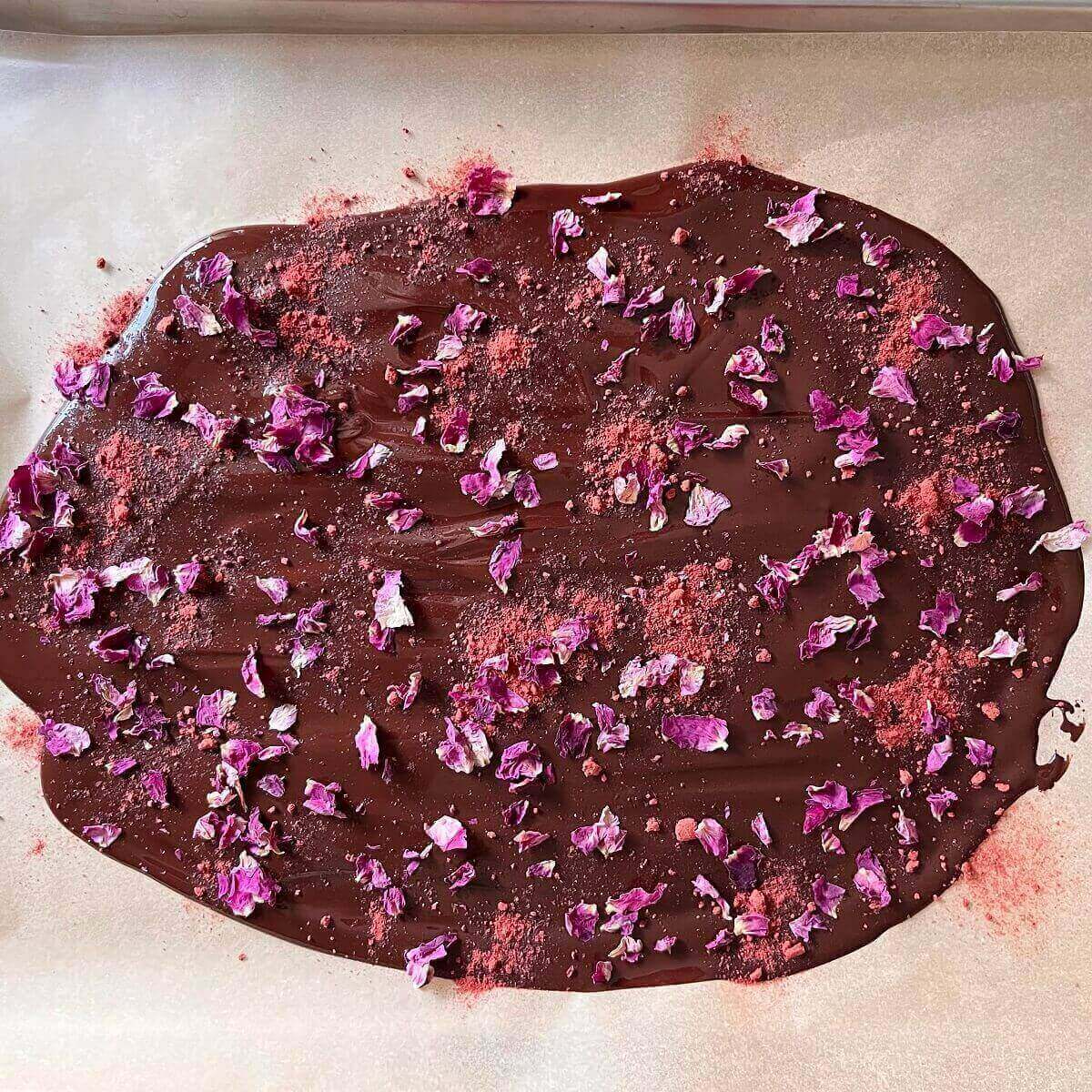 Melted chocolate spread on a sheet pan lined with parchment paper and topped with dried rose petals and strawberry powder.
