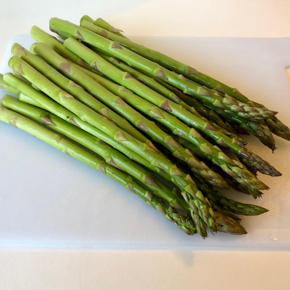 A pile of asparagus spears on a cutting board.