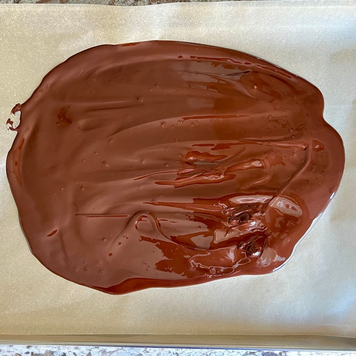 Melted chocolate spread on a sheet pan lined with parchment paper.