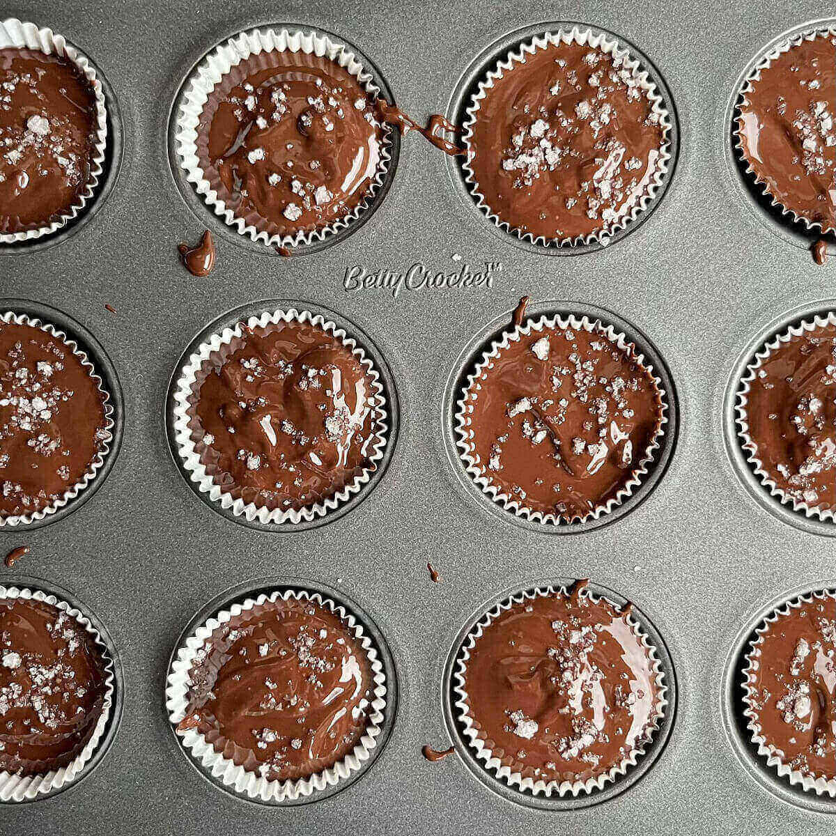 Liquid peanut butter cups sprinkled with sea salt in a mini muffin pan.