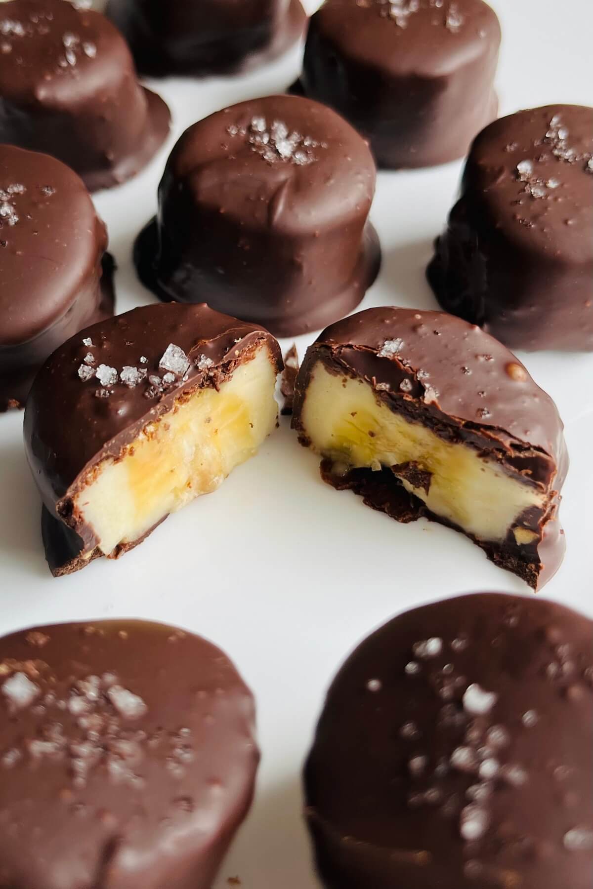 Peanut butter and chocolate dipped banana slices on a white plate.