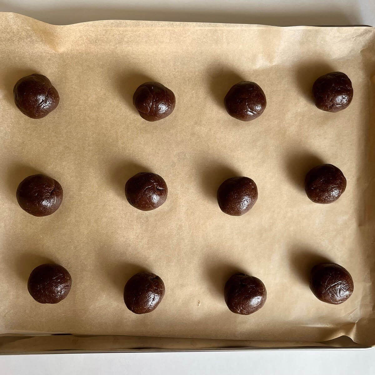 Carob dough balls on a sheet pan lined with parchment paper.