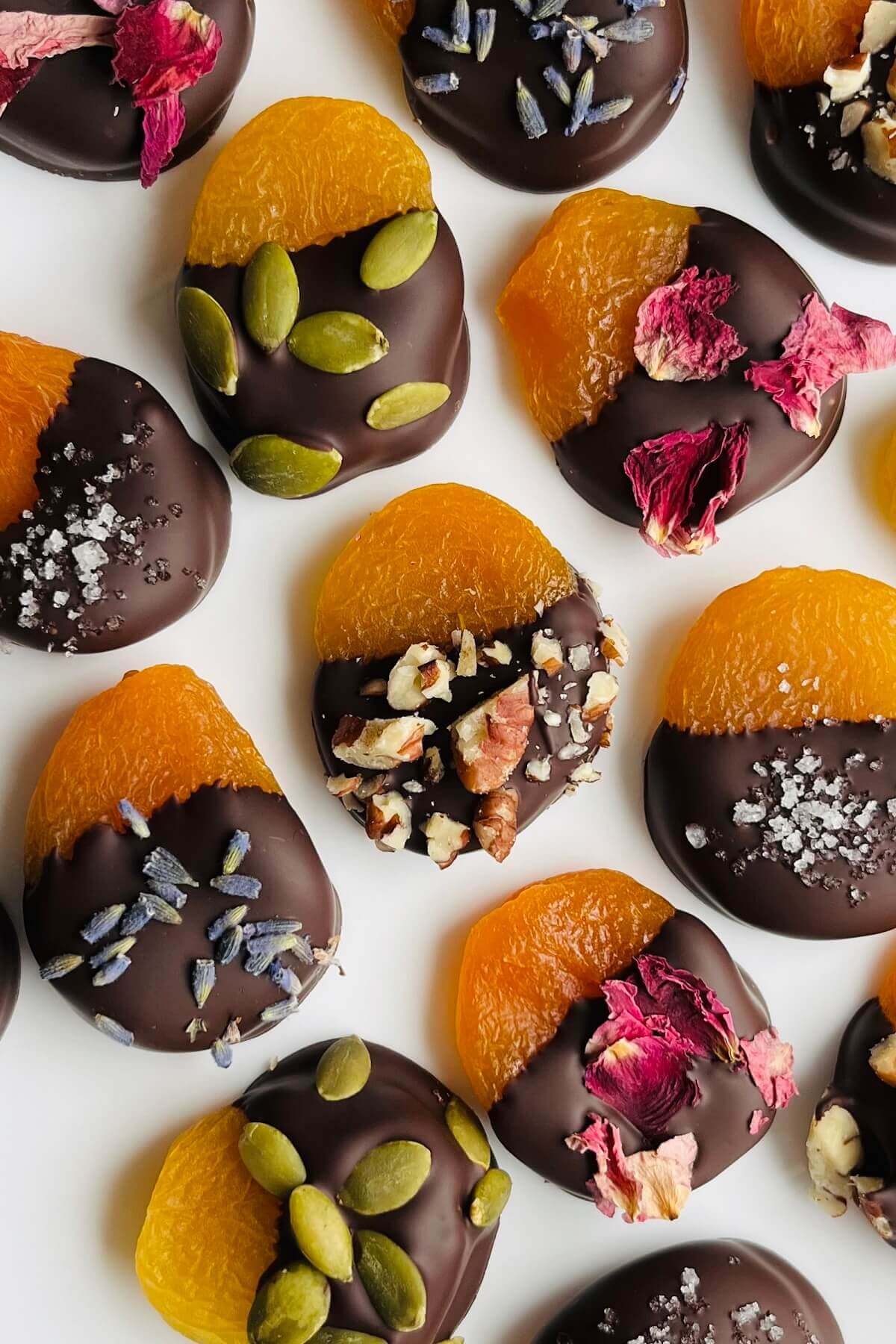 Chocolate dipped apricots with an assortment of different toppings on a white plate.