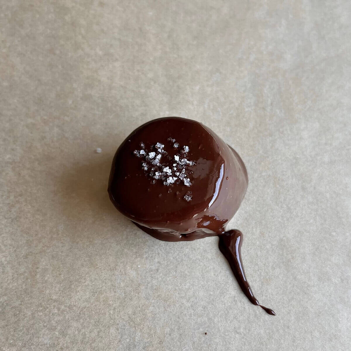 A chocolate coated banana slice sprinkled with sea salt on a sheet pan lined with parchment paper.