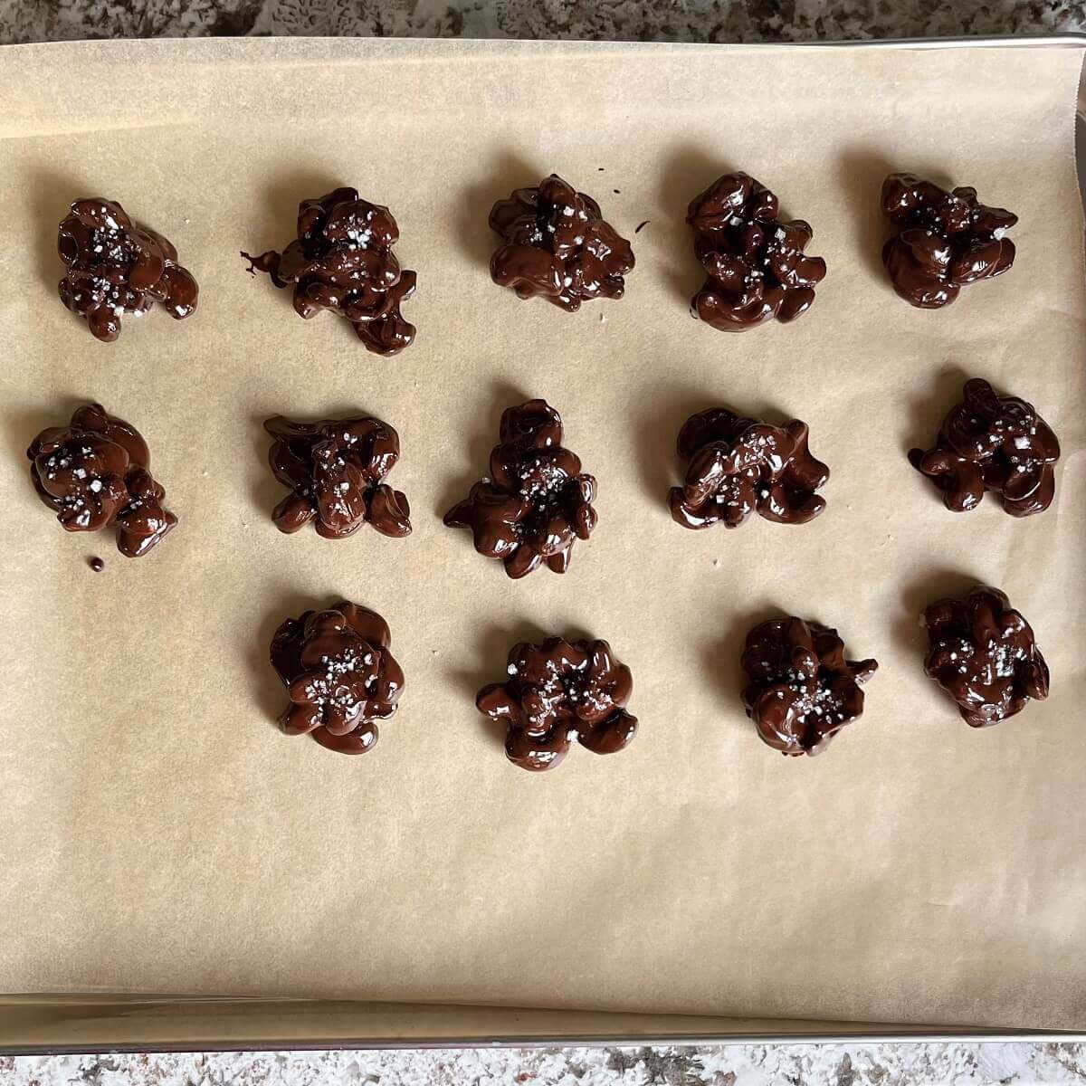Chocolate cashew clusters on a sheet pan lined with parchment paper.