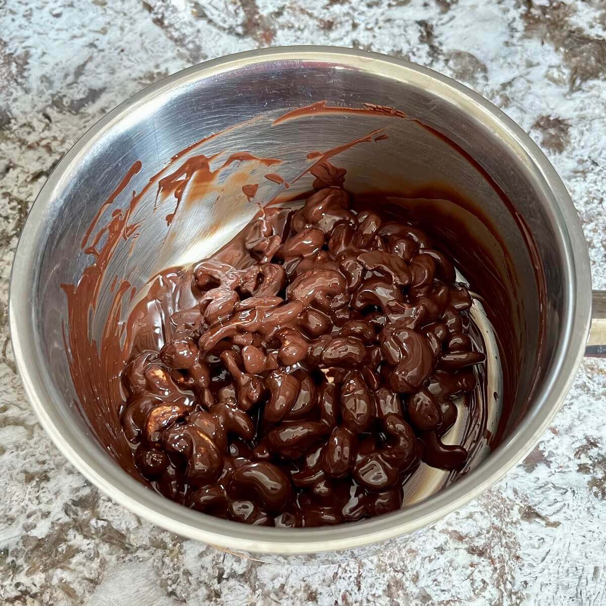 Melted dark chocolate and cashews in a steel pot.