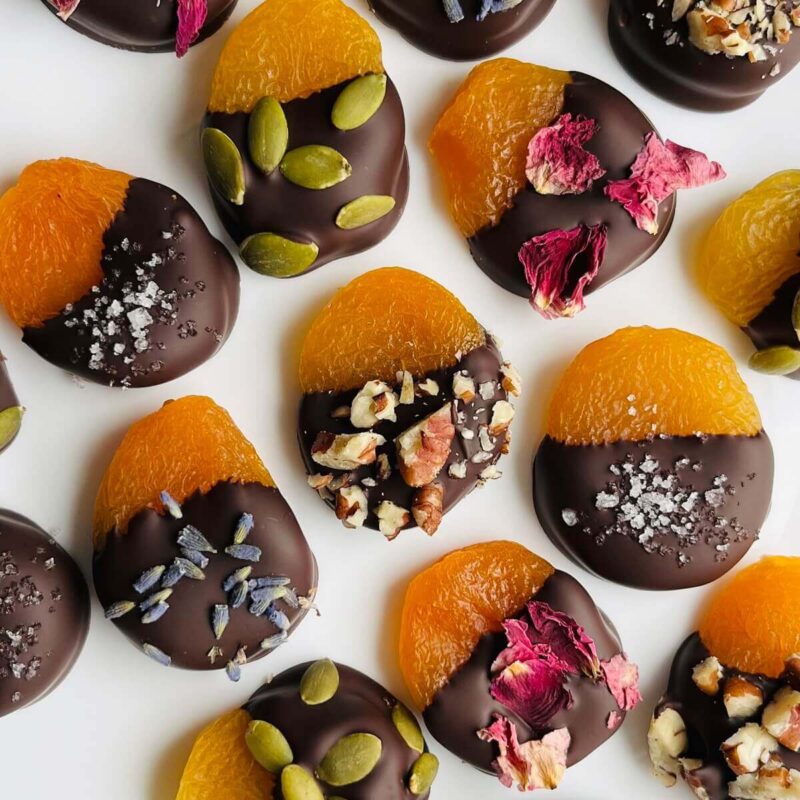 Apricots dipped in chocolate and sprinkled with edible flowers, seeds, and nuts.