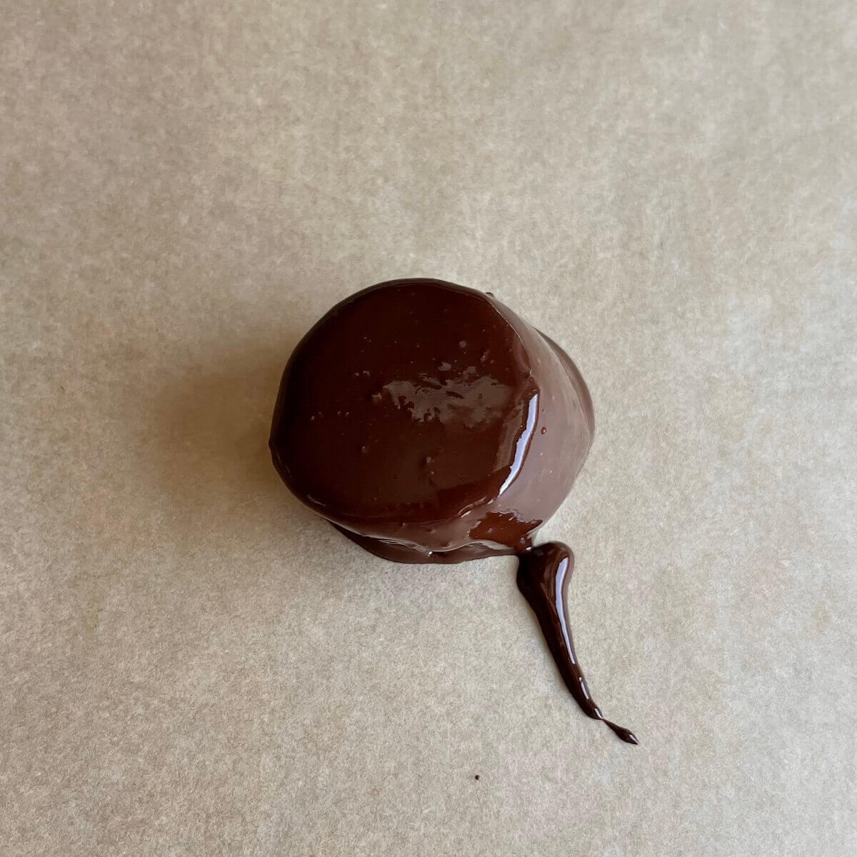 A slice of banana coated in melted chocolate on a sheet pan lined with parchment paper.