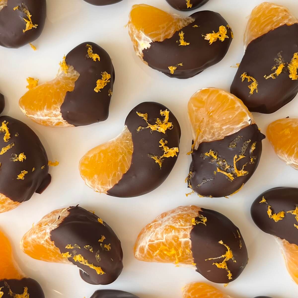 Chocolate dipped clementine oranges on a white plate.