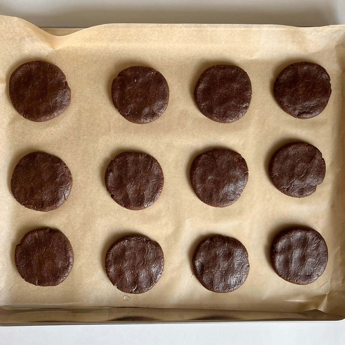 Raw cookies made with carob on a sheet pan lined with parchment paper.