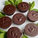 Vegan mint chocolates surrounded by fresh mint leaves on a white plate.