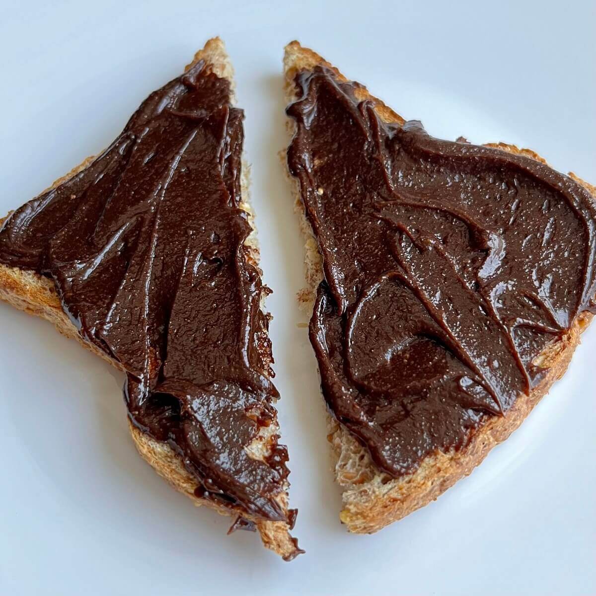 Two slices of toast with carob spread on a white plate.
