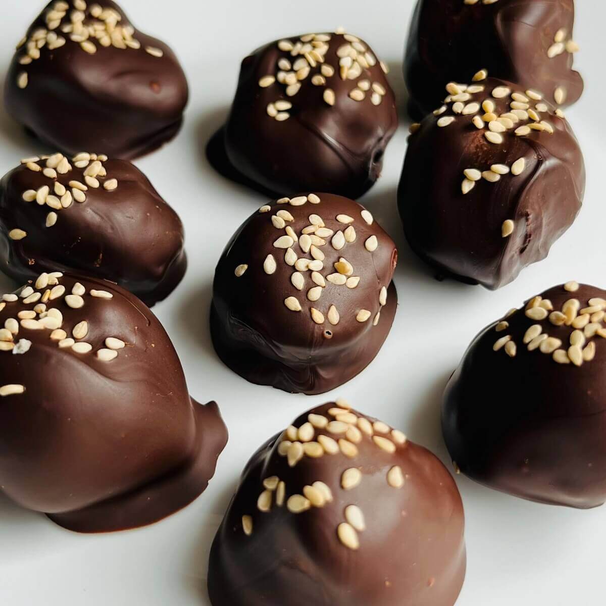 Tahini truffles sprinkled with sesame seeds on a white plate.