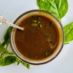 Balsamic basil vinaigrette in a glass bowl surrounded by basil leaves.