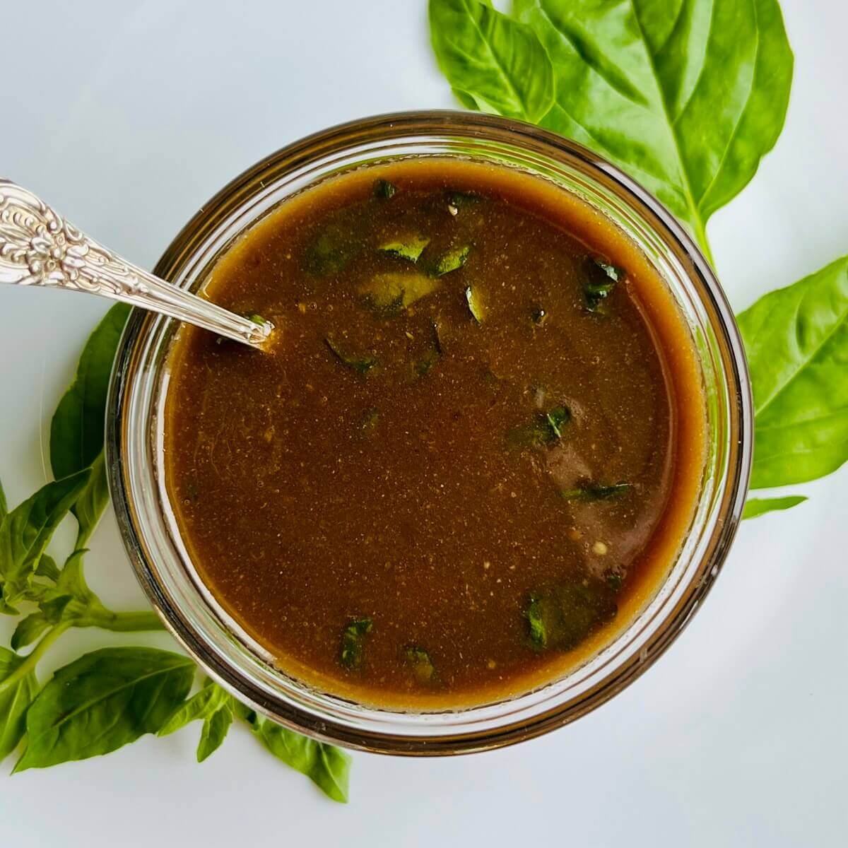 Vinaigrette in a glass bowl surrounded by basil leaves.