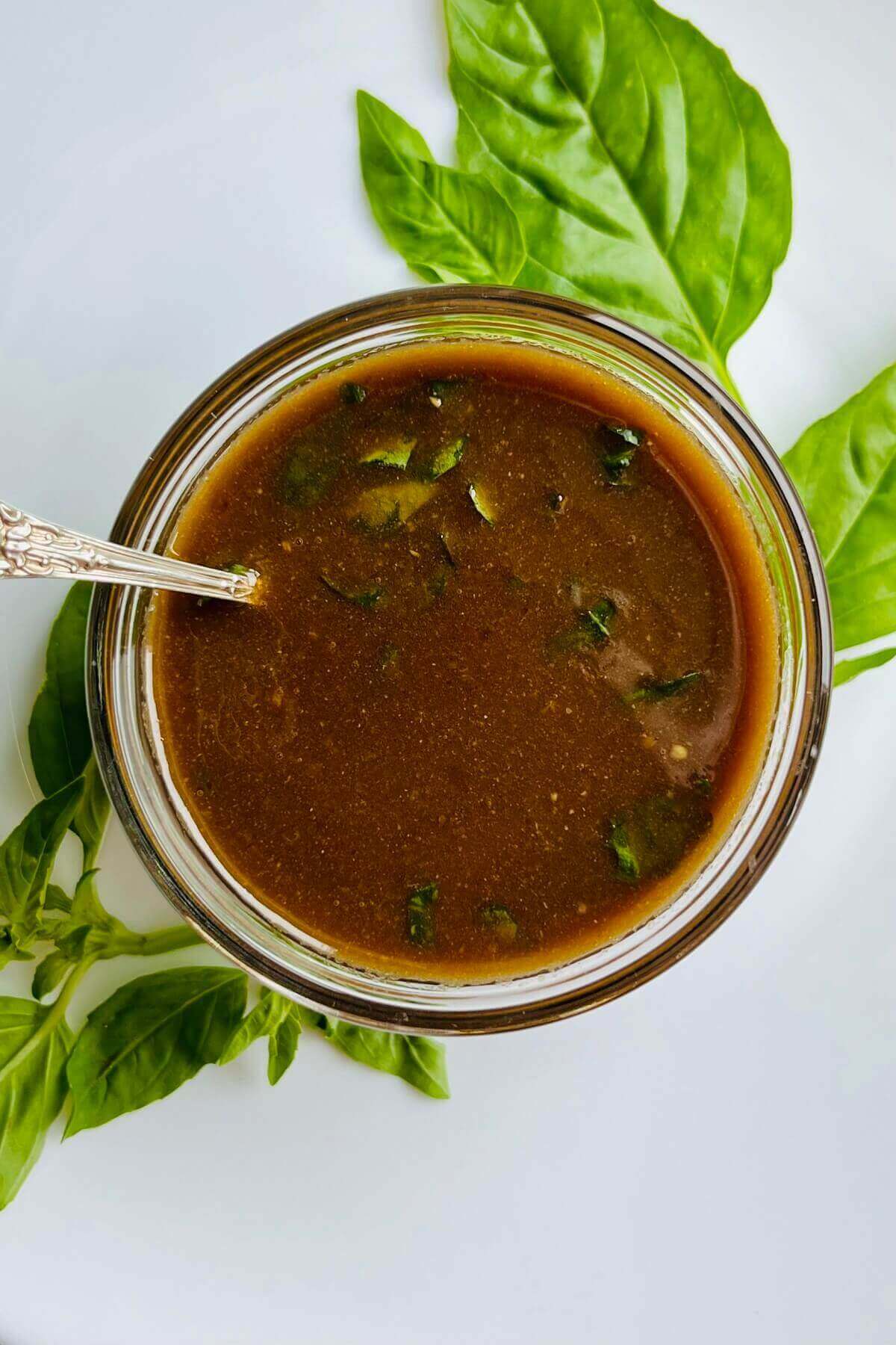 Basil balsamic salad dressing in a glass bowl next to some fresh basil leaves.