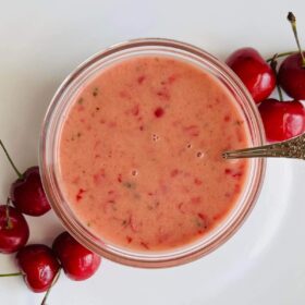 Cherry vinaigrette in a glass bowl with a silver spoon next to some fresh cherries.