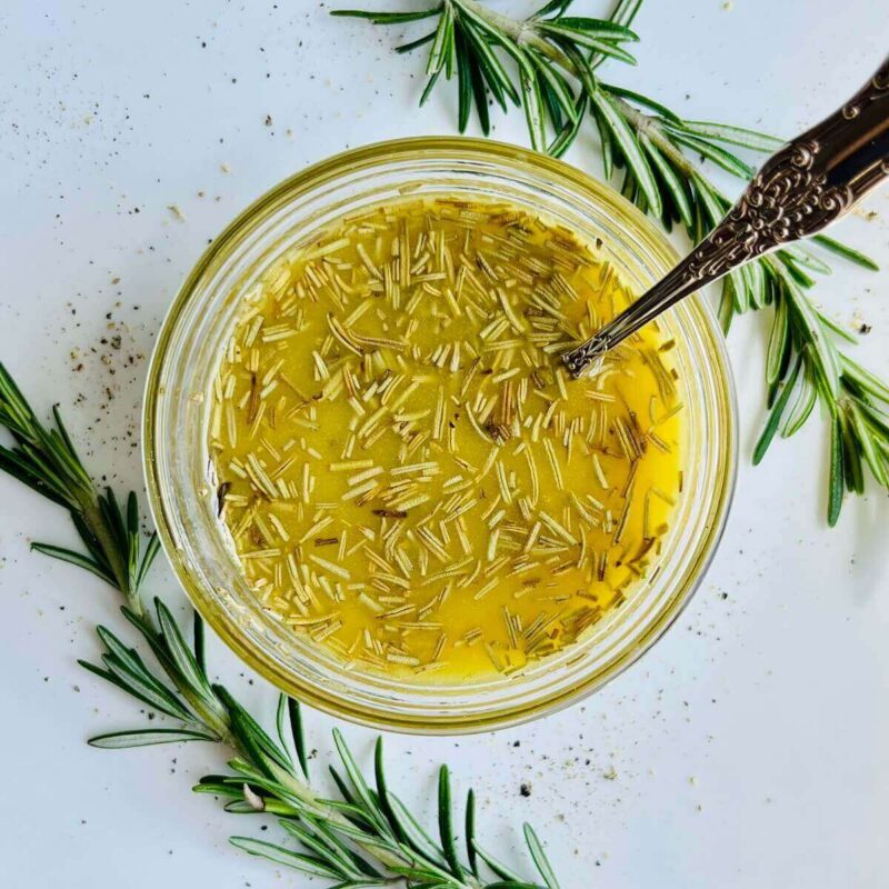 Vinaigrette in a glass bowl with an antique silver spoon surrounded by rosemary sprigs.