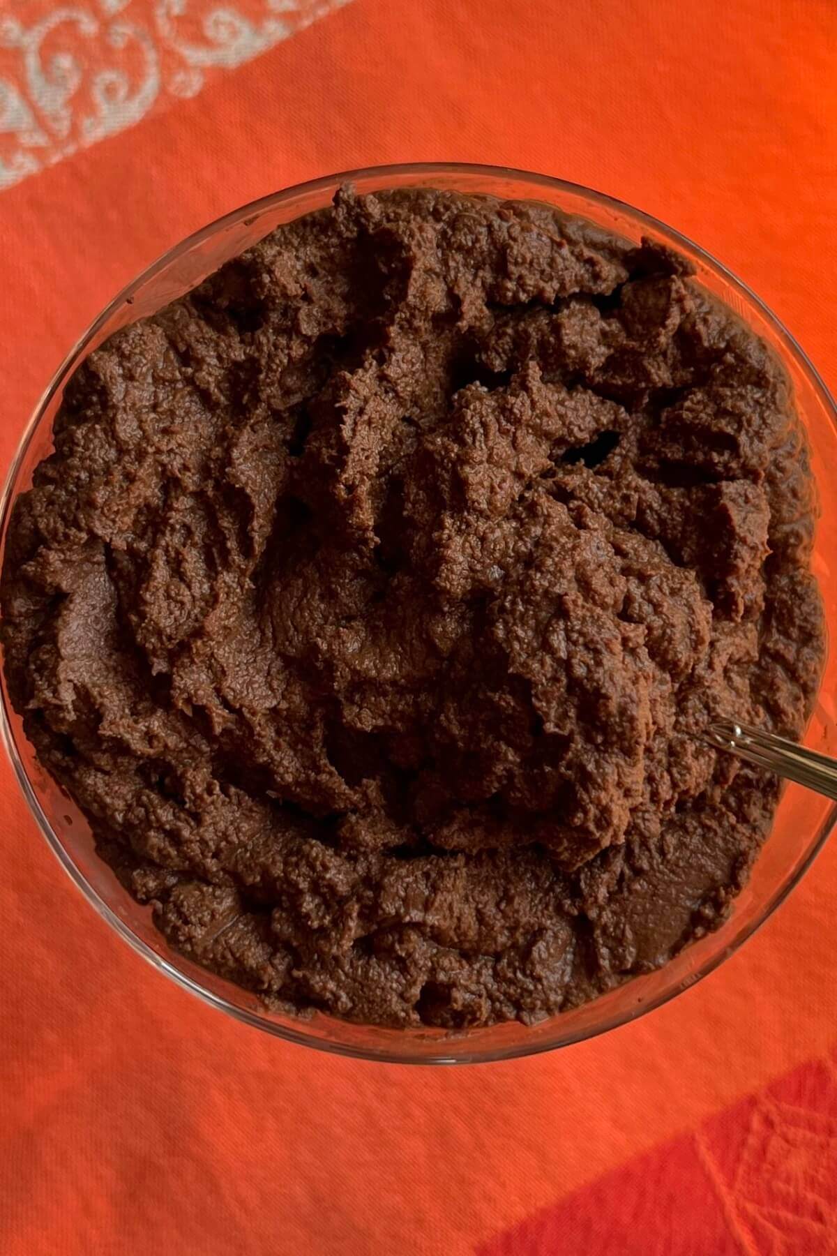 Chocolate mousse in a glass dish on an orange kitchen towel.