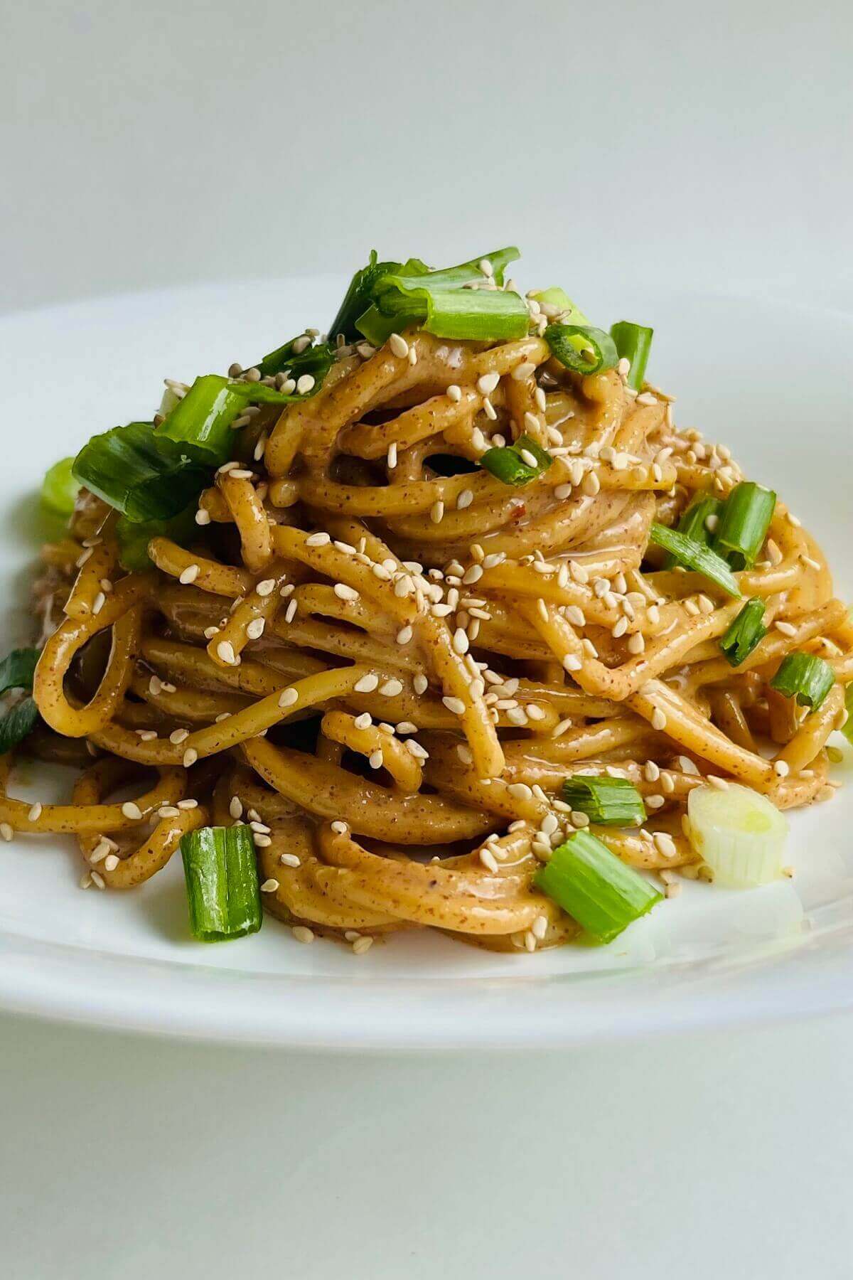 Noodles with almond butter sauce in a white bowl.