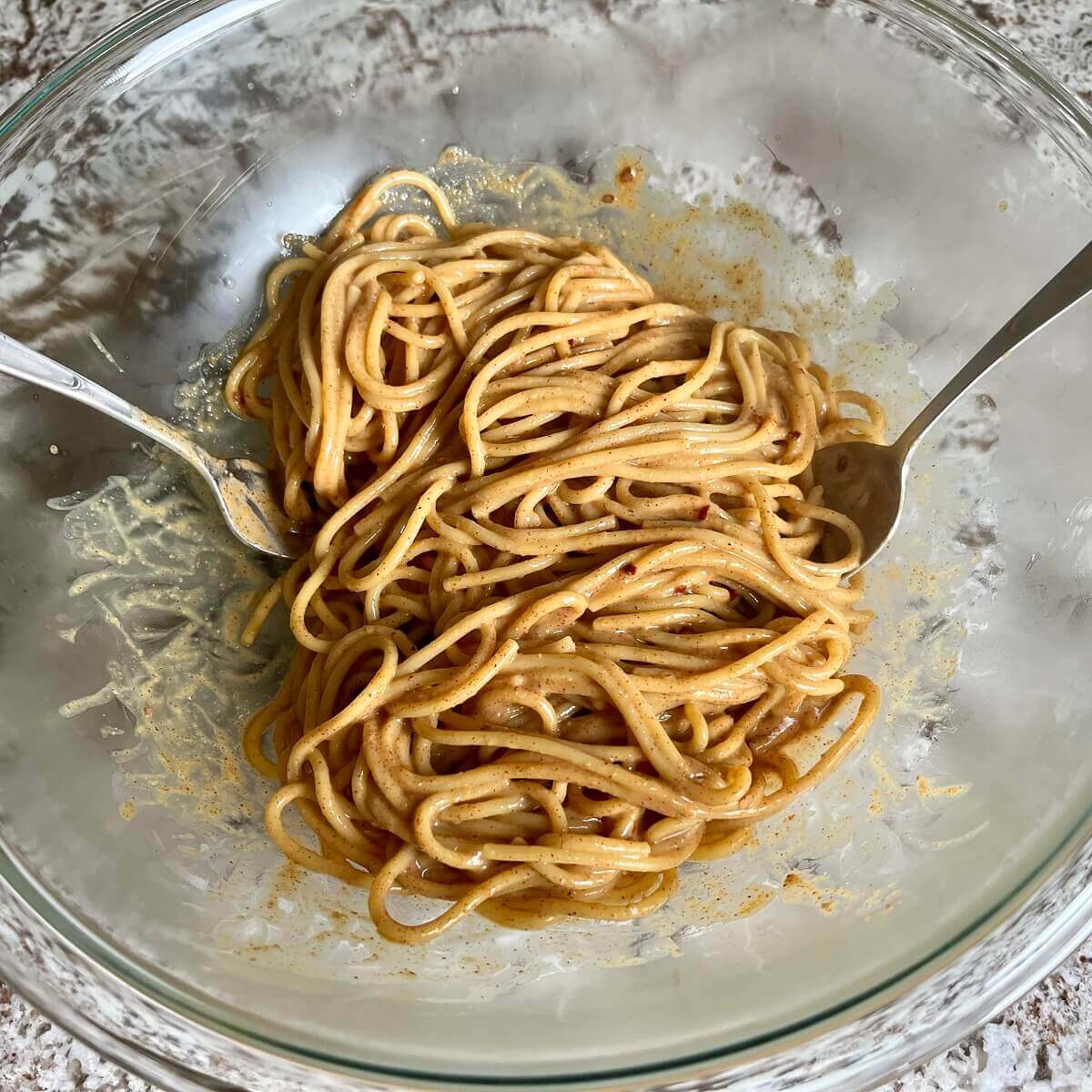 Noodles tossed with almond butter sauce in a glass bowl.