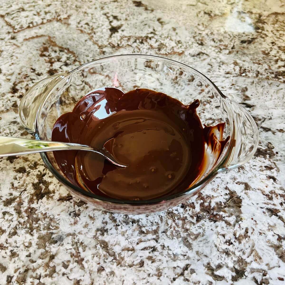 Melted dark chocolate and coconut oil in a glass bowl with a metal spoon.