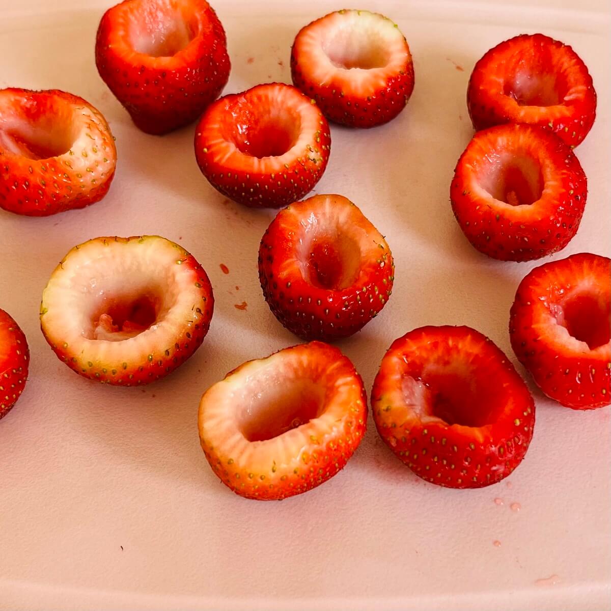 Hollowed out strawberries on a pink cutting board.