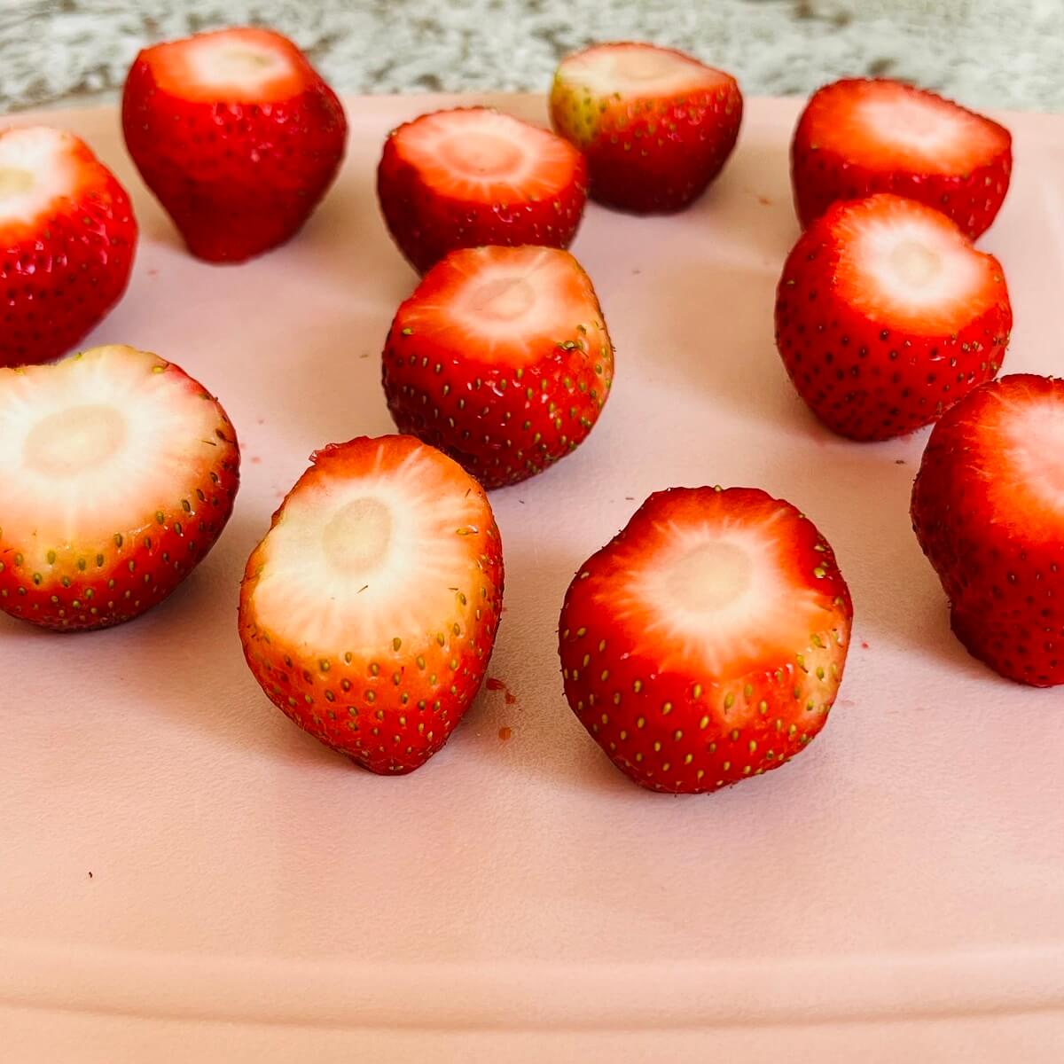 Strawberries with both ends sliced off on a cutting board.